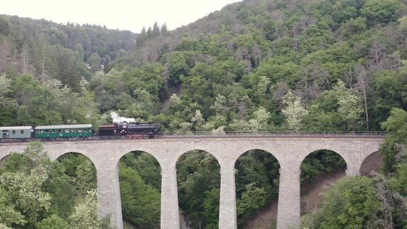 Steam train passing a stone viaduct in a valley,left to right,zoom.