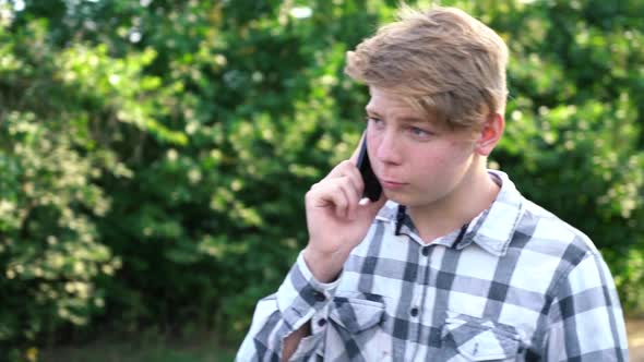 Young Caucasian Teenager Man in a Light Gray Checkered Shirt Speaks on the Phone