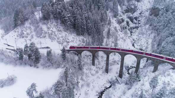 Viaduct and Train at Winter Day in Swiss Alps. Snowing. Switzerland. Aerial View