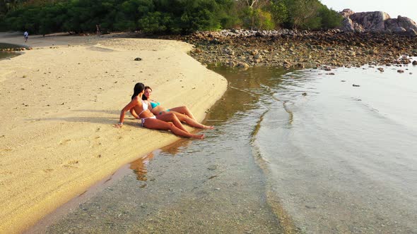 Pretty fun women on photoshoot enjoying life on the beach on clean white sand and blue 4K background