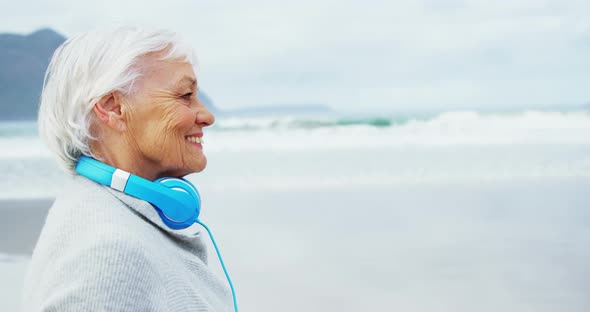 Senior woman wearing headphone around neck while walking on beach