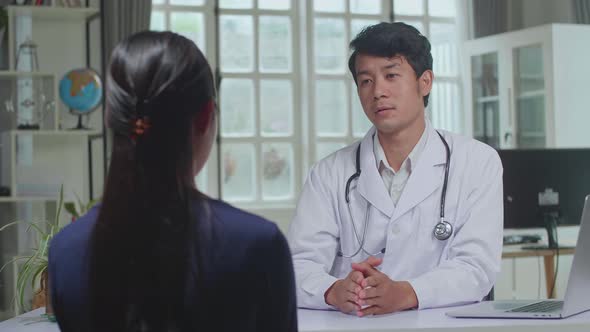 Asian Man Doctor Is Talking With Young Female Patient During Consultation In A Health Clinic