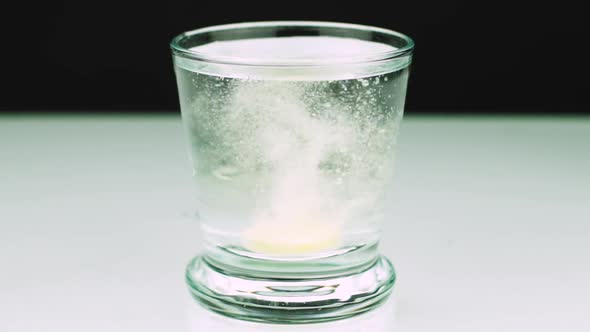 Close-up Shot of An Effervescent Tablet Against Pain Falls Into a Glass and Dissolves Slow-motion