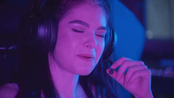 Young Pretty Woman Sitting in Neon Gaming Club - Wearing Big Headphones and Talking in Microphone