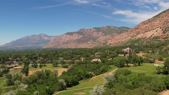 A drone shot of a golf course next to some mountains and located in the suburbs in the summer time