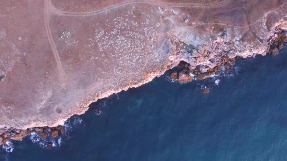 Top down aerial view of waves splash against rocky seashore, background. Flight over high cliffs of