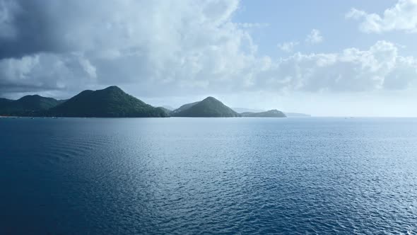 Drone camera approaches the mountains on the shore through the blue sea (Saint Lucia)