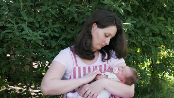 Mother with a Newborn Baby Walks in the Park. Young Mother Holds Her Baby in Her Arms. Breast