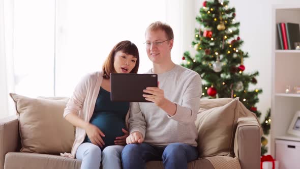 Man and Pregnant Woman with Tablet Pc on Christmas
