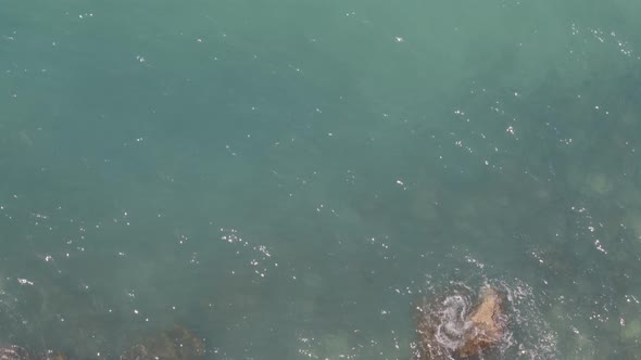 Top Down Aerial Pan from Waves Crashing on Rocks at Shore to Cliff in Greece