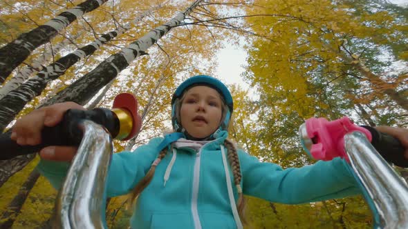 Portrait of Cheerful Little Girl in Safety Helmet Rides Bicycle in Woods POV