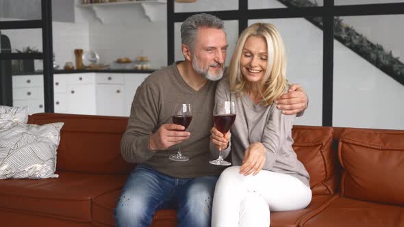 Happy Middleaged Wife and Husband Holding Glasses of Wine and Hugging at Home