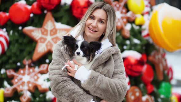 Beautiful Woman with Dog Papillon Near the Christmas Tree on the Street