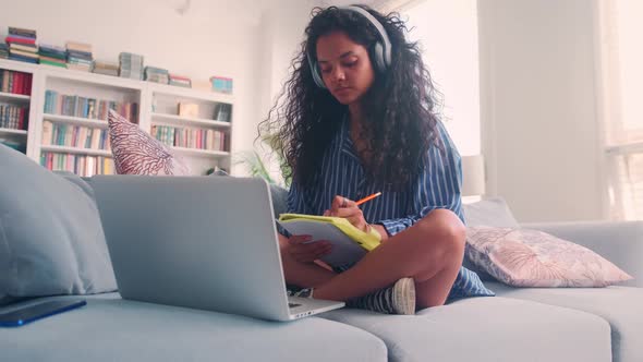 Young Indian Woman Student Listens to Online Lecture Sits on Sofa with Laptop