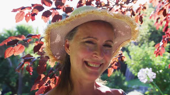 Portrait of happy caucasian senior woman in garden wearing sunhat and smiling in the sun