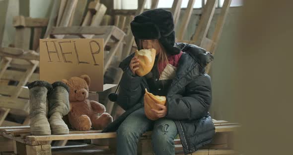 Portrait of a Homeless Girl with Dirty Face Eating Greedily the Loaf of Bread