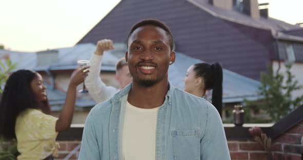 African American Looking at Camera Near His Satisfied Carefree Dancing Mixed Race Friends 