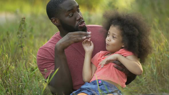 Funny dad and daughter making silly faces together, sitting in middle of grass