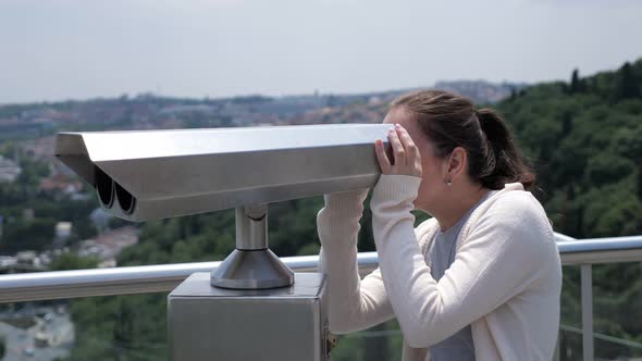 Woman Looks Through Binoculars Exploring Cityscape Along Bay