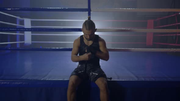 Attractive Boxer Reel Up Black Bandages for Kickboxing Before Fight Sitting Near Ring