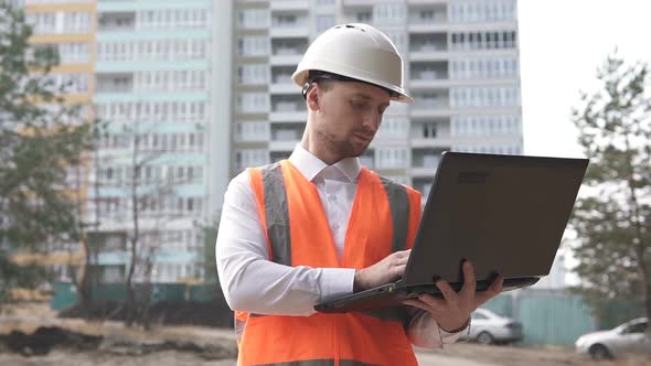 Construction Engineer Working on a Laptop Near a Construction Site