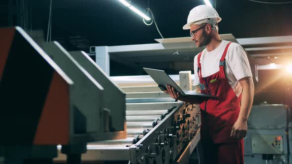 Side View of Engineer Watching Metal Working Process and Typing on Laptop