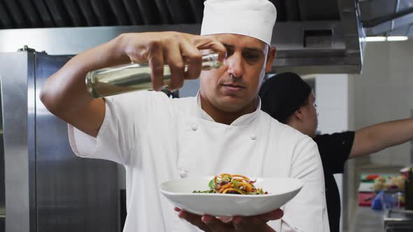 Caucasian male chef garnishing dish and smiling in restaurant kitchen