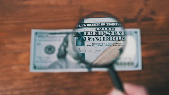 One Hundred Dollars Inspects Under Magnifying Glass on Wooden Table