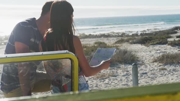 Caucasian couple standing near beach buggy by the sea reading a map