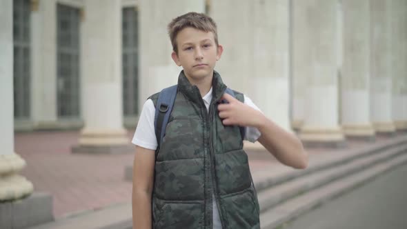 Camera Approaches To Confident Caucasian Brunette Schoolboy Posing Outdoors. Portrait of Boy