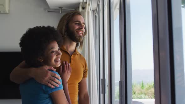 Mixed race couple looking out of the window at home