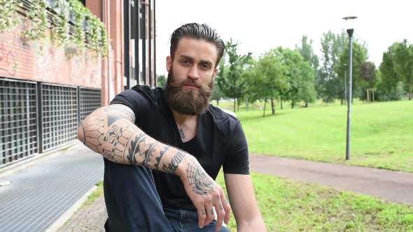 young beautiful bearded man sitting outdoor looking camera smiling