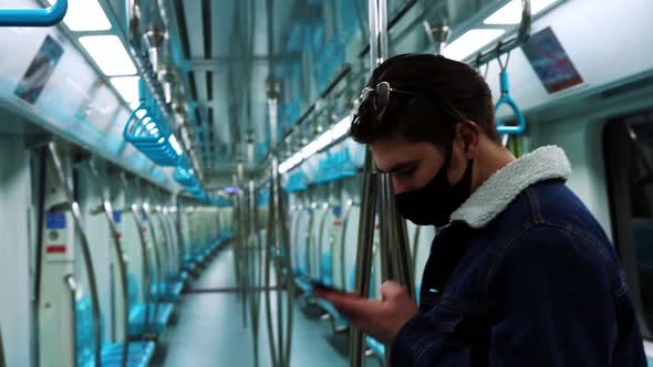 A Young Man in Black Mask Standing in Empty Subway Train and Looking at His Phone