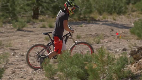 Teenage boy mountain biker walking with bike to top of trail.