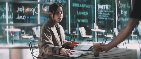 Young woman sitting in cafe with laptop at table taking a sip