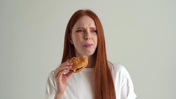 Closeup Portrait of Hungry Young Woman Eating Unappetizing Hamburger Dissatisfied with Food Quality