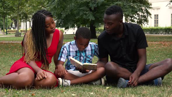 A Black Family Sits on Grass in a Park and Read a Book