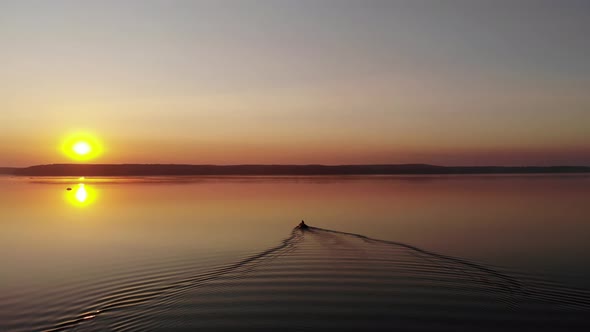 Shooting From a Drone of a Summer Sunset on a Large Lake Surrounded By Forests and Traces of a Motor