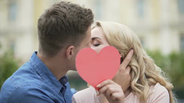 Couple kissing, girl putting up paper heart, young people in love, romantic