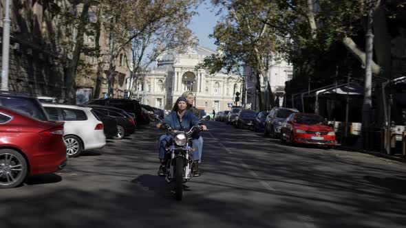 Two European Women Riding Motorcycle By the City Street