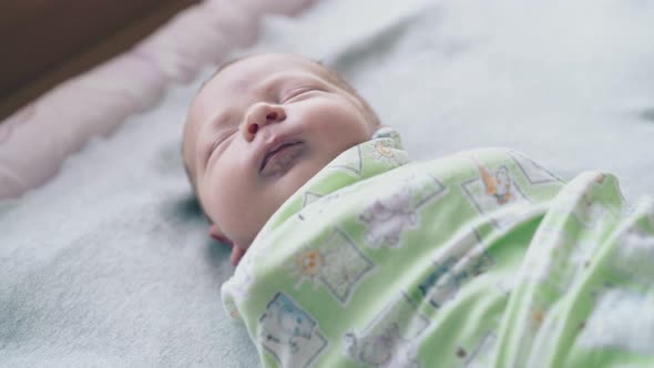 Newborn Baby Lies with Closed Eyes Wrapped in Muslin Swaddle