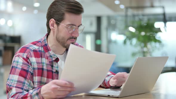 Serious Male Designer Working on Laptop with Documents 