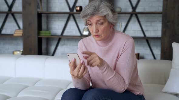 Sad Elderly Woman Sit on Sofa Hold Smartphone Feels Disappointed By Received Sms Bad News