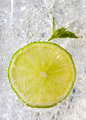 Macro photo of a piece of lime and mint leaf in a glass with ice and bubbles. Cold summer drink - PhotoDune Item for Sale