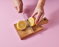Woman's hands cut a lemon on a wooden board with a knife around a pink background with copy - PhotoDune Item for Sale