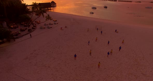 Aerial drone view of men playing soccer football on the beach of a tropical island at sunset.