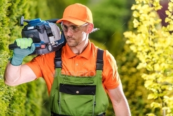 in His 30s with Gasoline Powerful Trimmer on His Shoulder. Garden Maintenance.