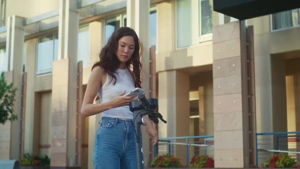 Brunette Woman Scanning Code Renting Scooter on Street