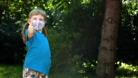 Little girl putting on a medical face mask and showing thumbs up gesture