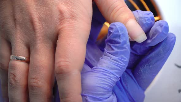 Close-up of manicure master in blue gloves filing nails with special nail file.